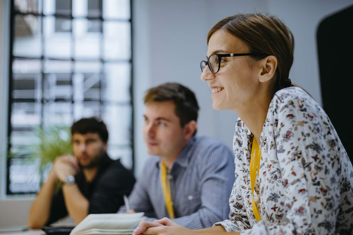 A woman in a flower blouse dives into learning, her smile reflecting the pursuit of knowledge with her peers.